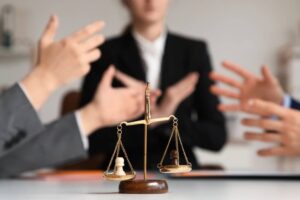 Justice scales on table against mediator with arguing clients in office, closeup