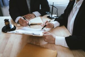 Lawyers reviewing and signing a legal contract at a desk with a gavel and scales of justice